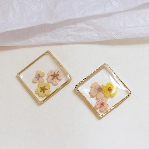 Dettaglio di pendenti in resina con fiori secchi rosa e gialli in cornici dorate