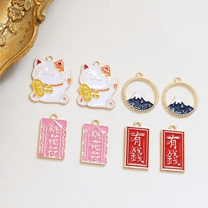Detail van kleurrijke emaille bedeltjes met Maneki Neko en perzikbloesem-amuletten voor DIY