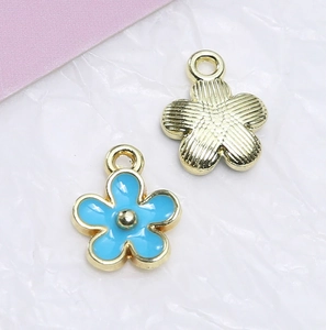 Makroaufnahme blauer Emaille-Blumenanhänger und goldene Charms für DIY-Schmuckherstellung