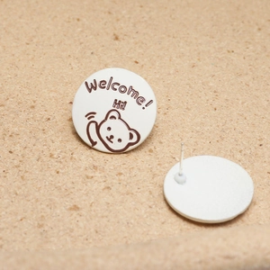 Macro view of round cartoon bear enamel stud earrings with Welcome text and silver pins