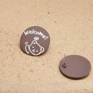Detailed view of round chocolate brown cartoon bear stud earrings with white welcome text