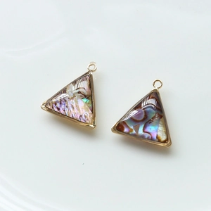 Détail macro de pendentifs triangles en nacre d'abalone avec cadres dorés géométriques