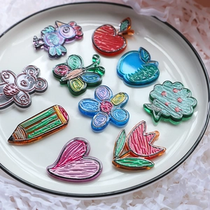 Flat lay of colorful hand-drawn acrylic charms featuring birds and flowers in a white dish