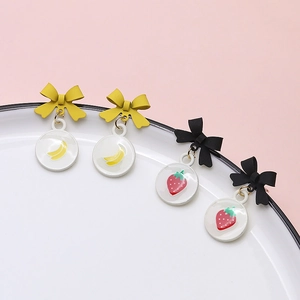 Detail of bow earrings with banana and strawberry charms in yellow and black matte