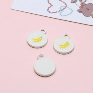 Detail of round white enamel charms with yellow banana pattern for DIY jewelry making