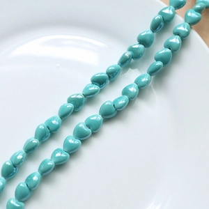 Macro shot of teal heart-shaped ceramic beads with glossy glaze for DIY jewelry making