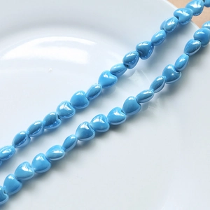 Detail of sky blue heart-shaped ceramic beads for DIY jewelry making on white tray