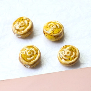Macro detail of four yellow ceramic flower beads with embossed roses for DIY jewelry