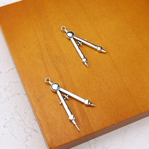 Detail of silver alloy compass charms for DIY jewelry making on wooden background