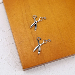 Detailed view of silver scissor-shaped jewelry pendants on an orange wooden surface
