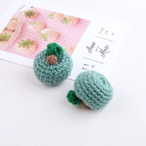 Detail of a handmade crochet green fruit pendant with a wool knit texture and leaf