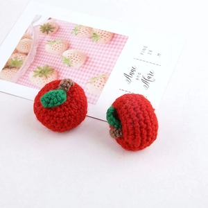 Macro shot of two handmade crochet red apple pendants with green leaves and knitted texture