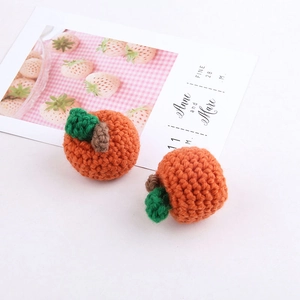 Close-up of handmade orange crochet pumpkin charms with green leaves and soft texture