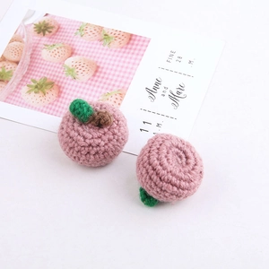 Close-up of handmade pink crochet apple accessories with green leaf and brown stem detail