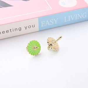 Close-up of green enamel umbrella earrings with gold plating on a pastel background