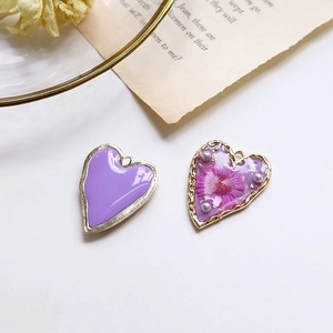 Dettaglio di ciondoli a cuore con fiori secchi, foglia d'oro e smalto viola