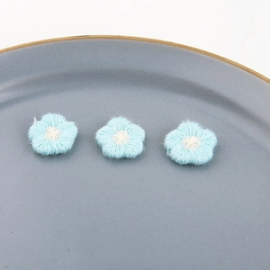 Detail van drie blauw geborduurde bloemenpatches met witte kernen op een keramische schaal