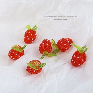 Handmade red beaded strawberry pendants with green leaves on white paper texture