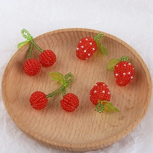 Handmade beaded cherry and strawberry charms displayed on a round wooden tray