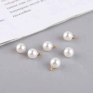 Detail of six round white faux pearl charms with golden bails for DIY jewelry making