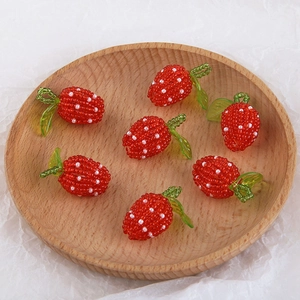 Detailed view of handmade beaded strawberry charms in a wooden tray for DIY jewelry