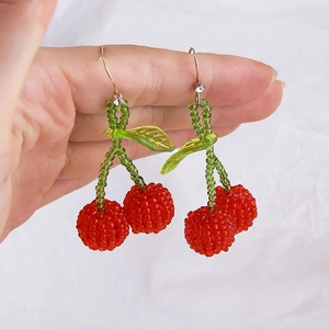 Macro detail of handmade beaded cherry earring with green leaves and gold metal hook