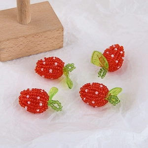 Close-up of four handmade beaded strawberry charms with green leaves for DIY jewelry