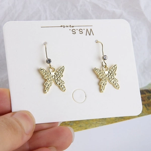 Detail von goldenen Schmetterlingsohrringen mit Kristallen auf weißer Karte