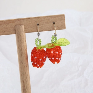 Detail of handcrafted beaded strawberry earrings with red crystals and green leaf accents