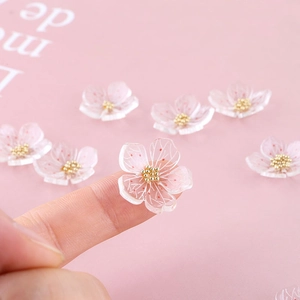 Macro detail of tiny translucent pink acrylic cherry blossom charms held on a fingertip
