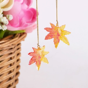 Handmade autumn gradient maple leaf earrings with gold chain in a rustic setting