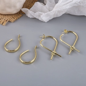 Detailed view of gold knot teardrop earrings and open curved hooks on textured linen fabric