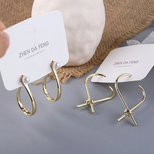 Close-up of golden teardrop pearl earrings and knotted heart studs on a display card