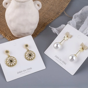 Detailed view of pearl bow earrings and gold letter pendants with rhinestones on a card