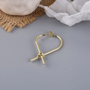 Close-up of golden metal knot stud earrings with a high-polished finish and minimalist design