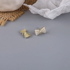 Detail of bow-shaped golden earrings with pearl inlay and DIY loops on textured background