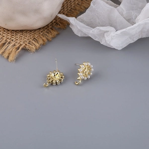 Detail of sunflower ear stud with N letter, white pearls and golden metallic finish