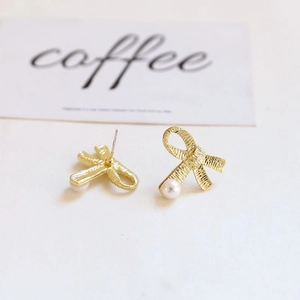 Detailed macro view of gold bow-knot earrings with a white pearl and brushed texture