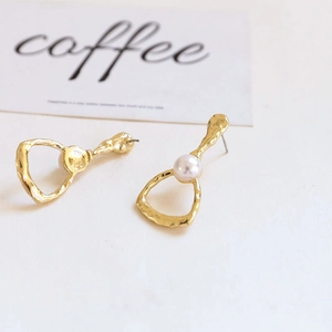 Detailed view of baroque gold-tone hammered metal earrings with central pearl accents