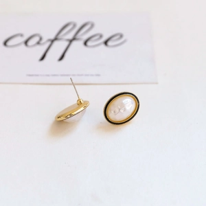 Macro detail of Baroque alloy pearl earrings with black enamel and gold gear texture