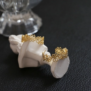 Detailed view of gold-plated daisy flower wreath C-shape earrings on a white prop