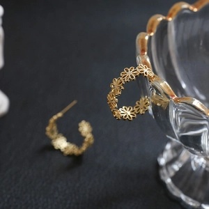 Detailed close-up of gold flower wreath C-shaped earrings on a glass bowl edge