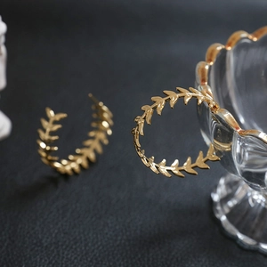 Detail of gold laurel leaf wreath C-shaped hoop earrings with metallic texture