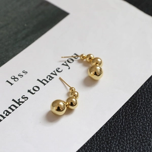 Macro detail of gold wreath C-shaped earrings with graduated polished metal beads