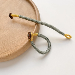 Detail of handcrafted grey and gold woven rope ring with wood button on a wooden plate