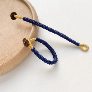 Macro shot of handmade dark blue and gold woven rope with a natural wooden bead fastener