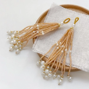 Detailed view of handmade beaded champagne tassels with white imitation pearls on linen