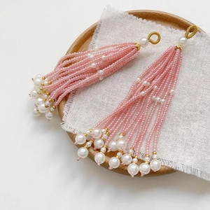 Close-up of handmade pink beaded tassel pendant with pearls and golden accents on linen