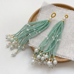 Detail of handmade beaded tassel earrings with green beads and white pearls on a tray