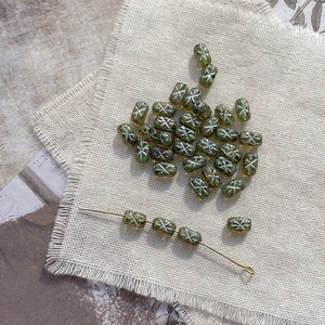 Macro view of vintage olive cylindrical glass beads with white X pattern on linen fabric